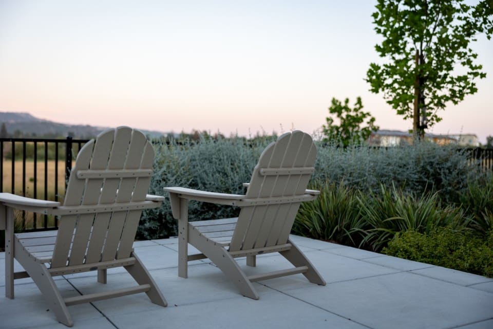Large-format slab patio with two Adirondack chairs and ornamental grasses